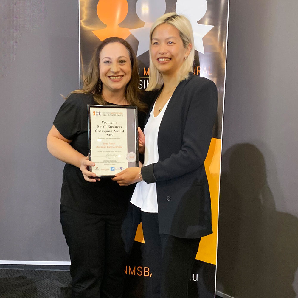 Two women smiling and holding a framed certificate at an award ceremony.