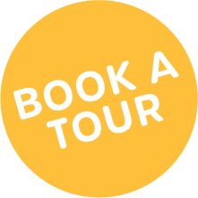 A circular yellow button with the text "Book a Tour" in white, capital letters.