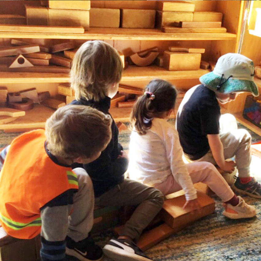 Four children sitting on wooden blocks in a cosy play area with wooden materials around them.