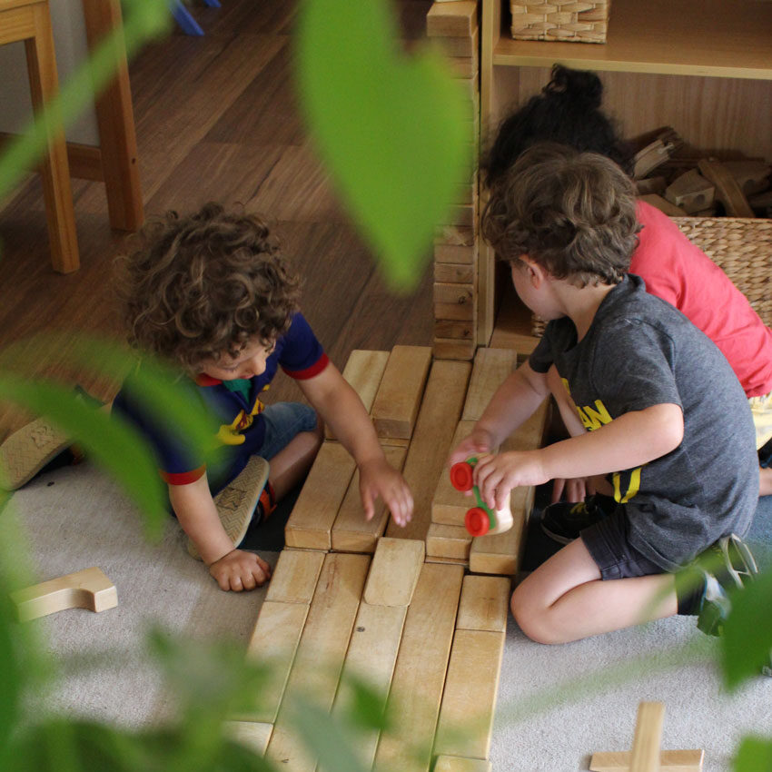 Three children playing together with wooden blocks in an indoor setting, focused on creative building.