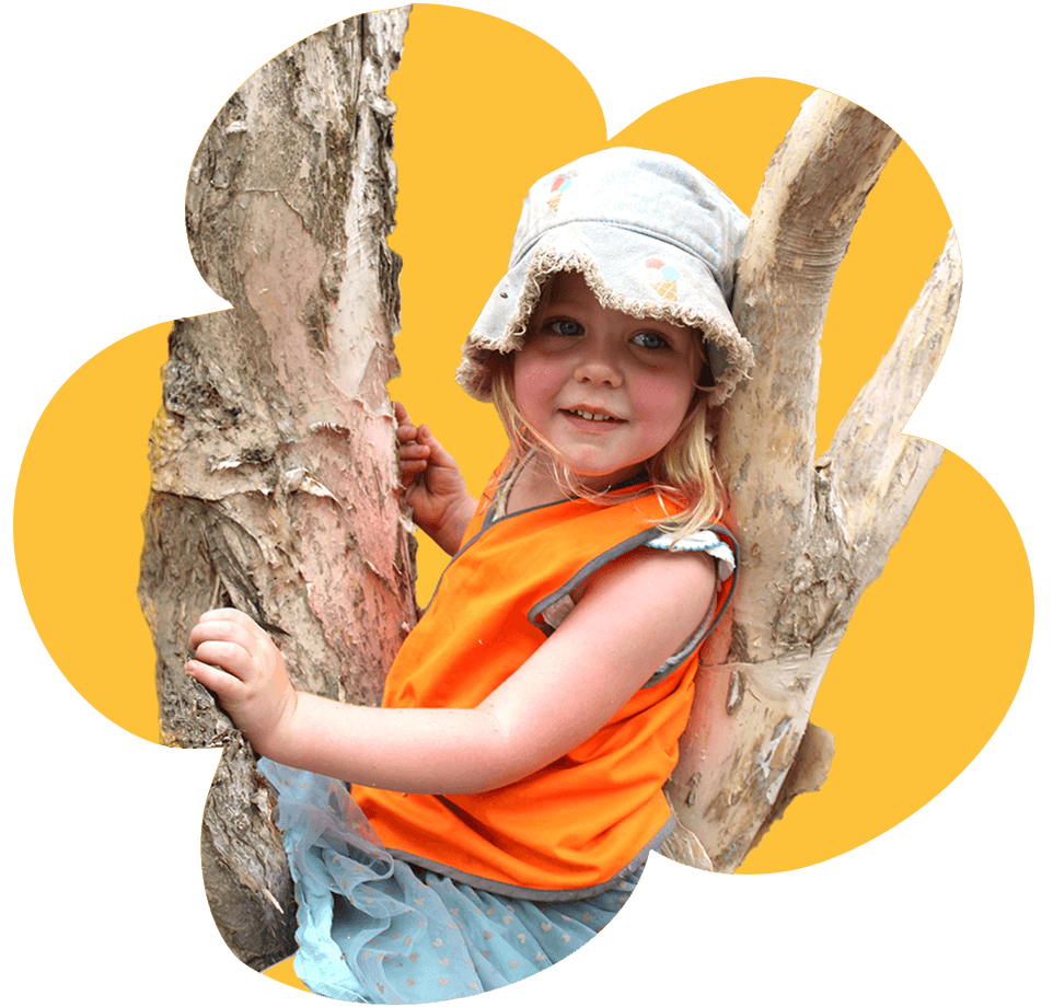 A young girl wearing a bucket hat and orange vest, happily sitting in a tree with a yellow background.