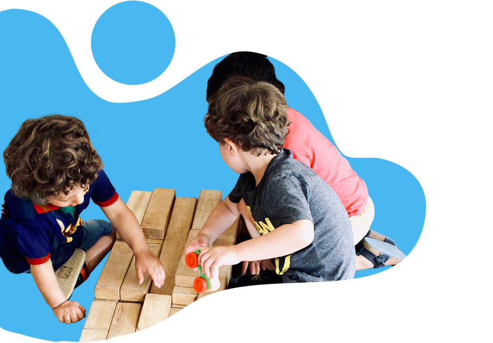 Three young boys are sitting on the floor, collaborating on building a structure using large wooden blocks.